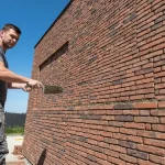 Montaż płytek klinkierowych na elewacji domu – pracownik przykładający płytkę szpachlą