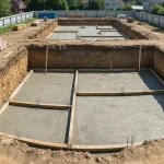 Rozkopany fundament domu z elementami budowy piwnice pod ziemią, widok z góry na wykopy i przygotowanie gruntu