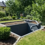Podziemny zbiornik na deszczówkę częściowo widoczny w ziemi z rynną odprowadzającą wodę, obok narzędzia montażowe