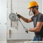 Pracownik odkładający stare płytki ceramiczne z ściany łazienki podczas pierwszego etapu remontu