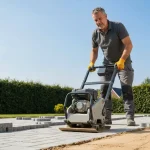 Pracownik ubija podłoże zagęszczarką wibracyjną przy brukach z kostki brukowej